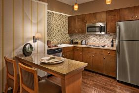 Sonesta Suites Scottsdale Gainey Ranch guest room kitchen, including table and two stools, oven and hob, microwave, and fridge-freezer.