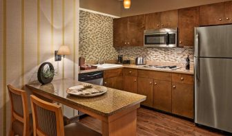 Sonesta Suites Scottsdale Gainey Ranch guest room kitchen, including table and two stools, oven and hob, microwave, and fridge-freezer.