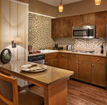 Sonesta Suites Scottsdale Gainey Ranch guest room kitchen, including table and two stools, oven and hob, microwave, and fridge-freezer.