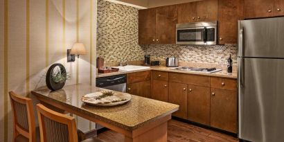 Sonesta Suites Scottsdale Gainey Ranch guest room kitchen, including table and two stools, oven and hob, microwave, and fridge-freezer.