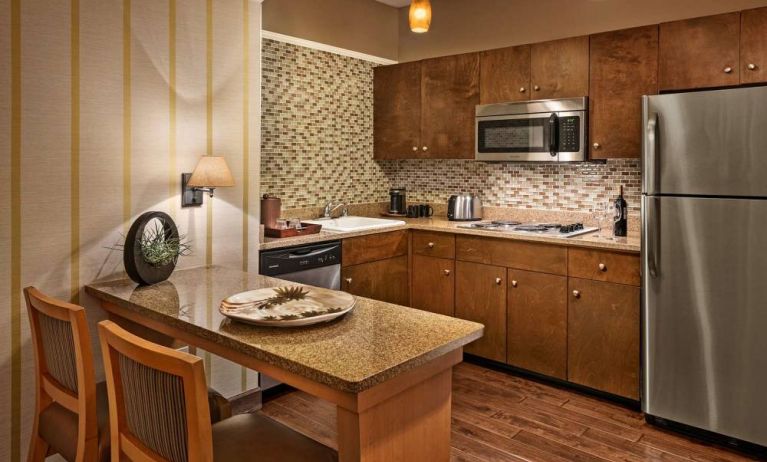 Sonesta Suites Scottsdale Gainey Ranch guest room kitchen, including table and two stools, oven and hob, microwave, and fridge-freezer.