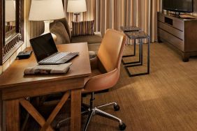 Sonesta Suites Scottsdale Gainey Ranch guest room workspace, furnished with desk, chair, and lamp, with TV and sofa nearby.