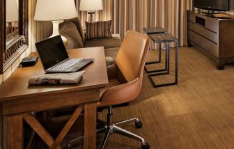 Sonesta Suites Scottsdale Gainey Ranch guest room workspace, furnished with desk, chair, and lamp, with TV and sofa nearby.