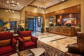 Sonesta Suites Scottsdale Gainey Ranch’s lobby has many potted plants, including cacti, a marble floor, and comfortable armchairs around a coffee table.