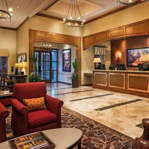 Sonesta Suites Scottsdale Gainey Ranch’s lobby has many potted plants, including cacti, a marble floor, and comfortable armchairs around a coffee table.