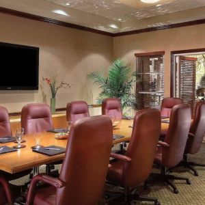 Meeting room in Sonesta Suites Scottsdale Gainey Ranch, furnished with long wooden table, 10 leather chairs, and a wall-mounted widescreen television.