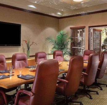 Meeting room in Sonesta Suites Scottsdale Gainey Ranch, furnished with long wooden table, 10 leather chairs, and a wall-mounted widescreen television.