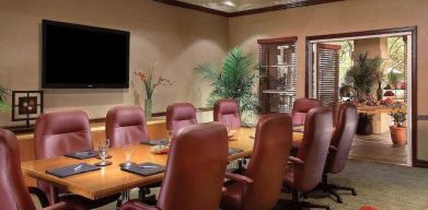 Meeting room in Sonesta Suites Scottsdale Gainey Ranch, furnished with long wooden table, 10 leather chairs, and a wall-mounted widescreen television.