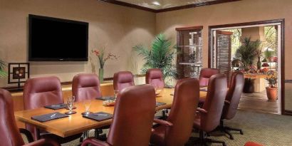 Meeting room in Sonesta Suites Scottsdale Gainey Ranch, furnished with long wooden table, 10 leather chairs, and a wall-mounted widescreen television.