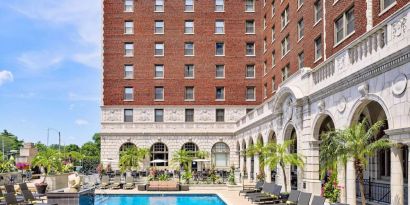 The Chase Park Plaza Royal Sonesta St. Louis’ outdoor pool has rows of sun loungers and potted palm trees by the side, plus sofa seating and a nearby patio.