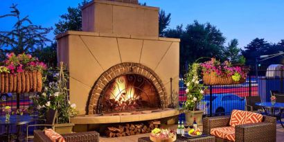 The outdoor fireplace at The Chase Park Plaza Royal Sonesta St. Louis has comfortable sofa and armchair seating nearby, in addition to coffee tables and beautiful flowers.