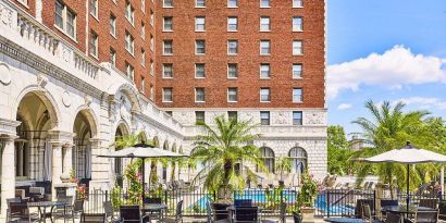 The hotel patio features tables and chairs, some shaded, overlooking the outdoor pool.