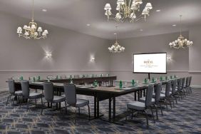 Meeting room in The Chase Park Plaza Royal Sonesta St. Louis, featuring long tables arranged in a U-shape, quartet of chandeliers, seating for over a dozen, and a projector screen.