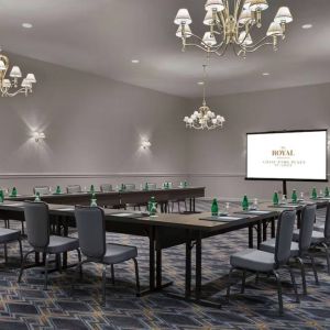 Meeting room in The Chase Park Plaza Royal Sonesta St. Louis, featuring long tables arranged in a U-shape, quartet of chandeliers, seating for over a dozen, and a projector screen.