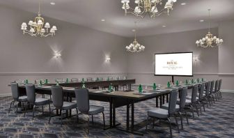 Meeting room in The Chase Park Plaza Royal Sonesta St. Louis, featuring long tables arranged in a U-shape, quartet of chandeliers, seating for over a dozen, and a projector screen.