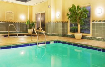 Sonesta Atlanta Airport South’s indoor pool has a hot tub nearby, potted plants by the side, and large windows.