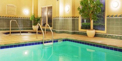 Sonesta Atlanta Airport South’s indoor pool has a hot tub nearby, potted plants by the side, and large windows.