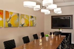 Sonesta Atlanta Airport South meeting room, furnished with long wooden table surrounded by swivel chairs, and art and a widescreen TV on the walls.