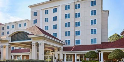 Sonesta Atlanta Airport South’s exterior features a covered entrance, well-kept greenery, and stylish red roof tiles.