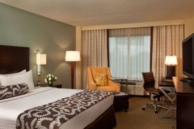 Double bed guest room in Sonesta Atlanta Airport North, featuring TV, window, armchair, and workspace desk and chair.