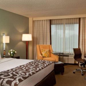 Double bed guest room in Sonesta Atlanta Airport North, featuring TV, window, armchair, and workspace desk and chair.