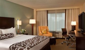 Double bed guest room in Sonesta Atlanta Airport North, featuring TV, window, armchair, and workspace desk and chair.