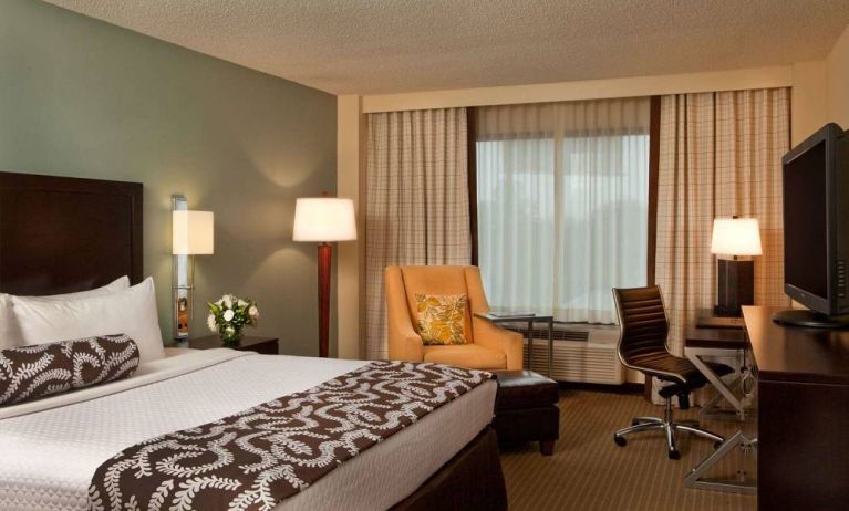 Double bed guest room in Sonesta Atlanta Airport North, featuring TV, window, armchair, and workspace desk and chair.