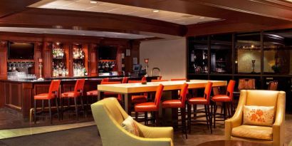 The hotel’s lobby lounge includes armchairs surrounding a coffee table, plus a bar with tall red stools and assorted refreshments.