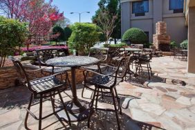 Sonesta Atlanta Airport North’s patio has tables and chairs beside flowers, bushes, and trees.