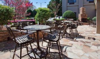 Sonesta Atlanta Airport North’s patio has tables and chairs beside flowers, bushes, and trees.