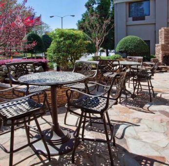 Sonesta Atlanta Airport North’s patio has tables and chairs beside flowers, bushes, and trees.