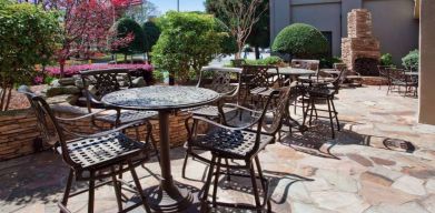 Sonesta Atlanta Airport North’s patio has tables and chairs beside flowers, bushes, and trees.