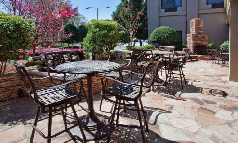 Sonesta Atlanta Airport North’s patio has tables and chairs beside flowers, bushes, and trees.