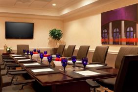 Meeting room in Sonesta Atlanta Airport North, furnished with long wooden table, a dozen chairs, and art and a widescreen television on the walls.