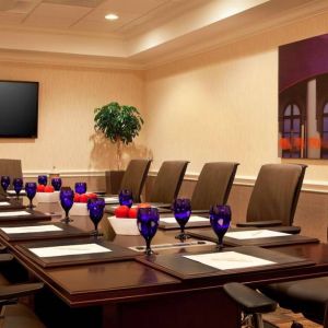 Meeting room in Sonesta Atlanta Airport North, furnished with long wooden table, a dozen chairs, and art and a widescreen television on the walls.