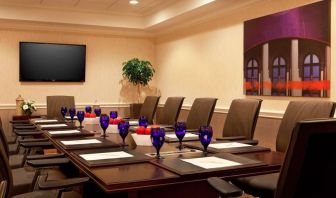 Meeting room in Sonesta Atlanta Airport North, furnished with long wooden table, a dozen chairs, and art and a widescreen television on the walls.