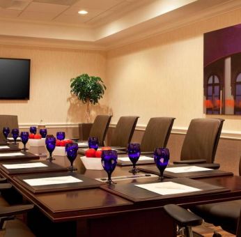 Meeting room in Sonesta Atlanta Airport North, furnished with long wooden table, a dozen chairs, and art and a widescreen television on the walls.