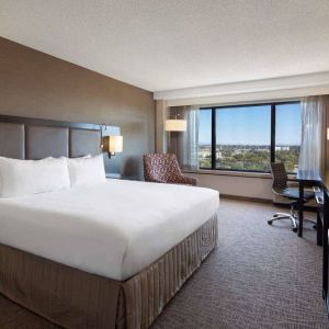 Double bed guest room Sonesta San Jose, with workspace desk and chair, armchair, TV, and window.