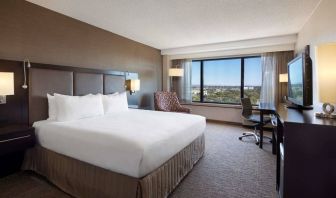 Double bed guest room Sonesta San Jose, with workspace desk and chair, armchair, TV, and window.