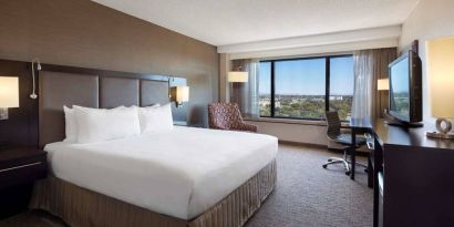 Double bed guest room Sonesta San Jose, with workspace desk and chair, armchair, TV, and window.