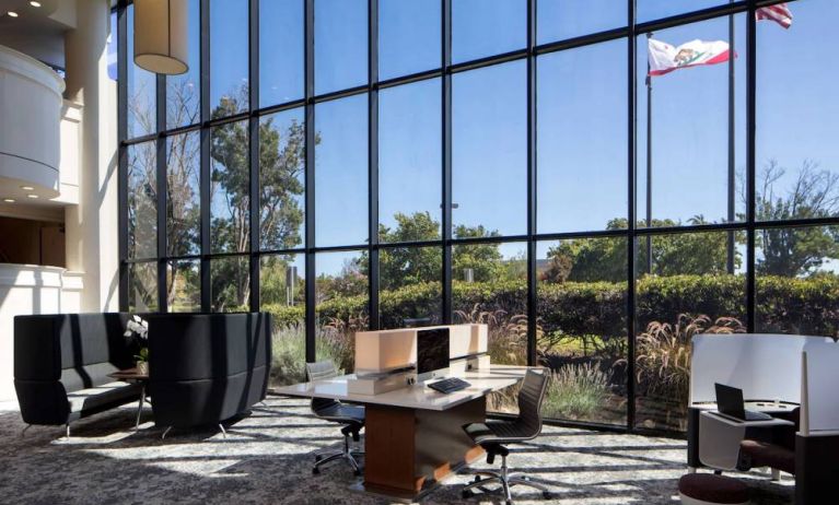 The hotel’s business center has a wall of windows next to it with a view of greenery and flags, while the center itself features multiple workstations and nooks for guests to use.