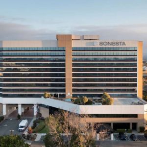 Sonesta San Jose’s exterior has ample parking for guests, abundant greenery, and a pool, plus the hotel chain’s name on the outside of the top floor.