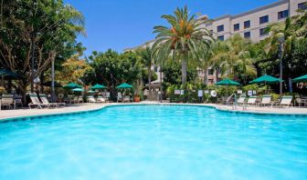 The outdoor pool at Sonesta ES Suites Anaheim Resort Area features nearby sun loungers and shaded tables and chairs, with numerous trees close by.