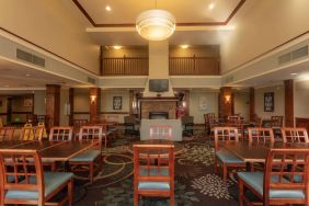 The hotel breakfast area has a high ceiling, wide range of table sizes, carpeted floor, and a wall-mounted TV.