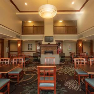 The hotel breakfast area has a high ceiling, wide range of table sizes, carpeted floor, and a wall-mounted TV.