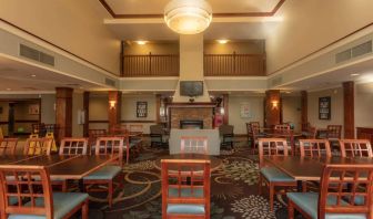 The hotel breakfast area has a high ceiling, wide range of table sizes, carpeted floor, and a wall-mounted TV.