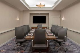 Sonesta Charlotte Executive Park meeting room, furnished with long table, a dozen leather swivel chairs, and a large, wall-mounted TV.