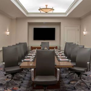 Sonesta Charlotte Executive Park meeting room, furnished with long table, a dozen leather swivel chairs, and a large, wall-mounted TV.