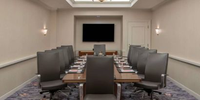 Sonesta Charlotte Executive Park meeting room, furnished with long table, a dozen leather swivel chairs, and a large, wall-mounted TV.