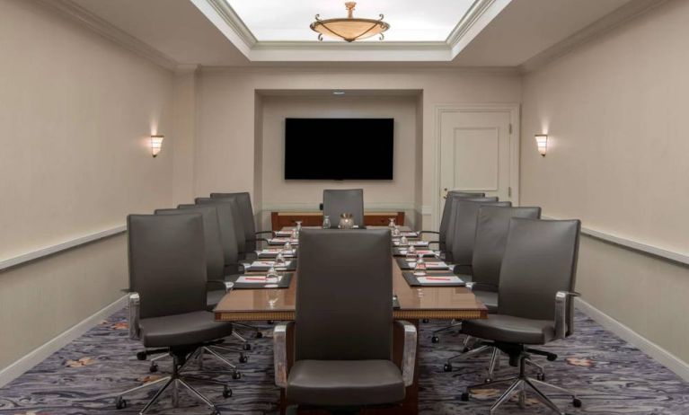 Sonesta Charlotte Executive Park meeting room, furnished with long table, a dozen leather swivel chairs, and a large, wall-mounted TV.